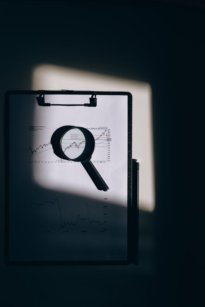 A magnifying glass lays over a financial chart on a clipboard, casting intriguing shadows.